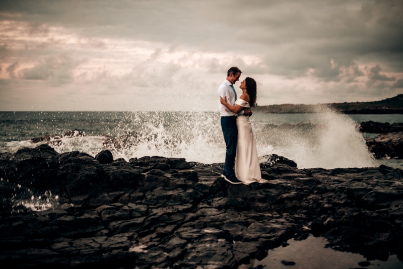 Elopement Photographer, bride and groom gaze at each other as ocean waves crash on the rocks behind them